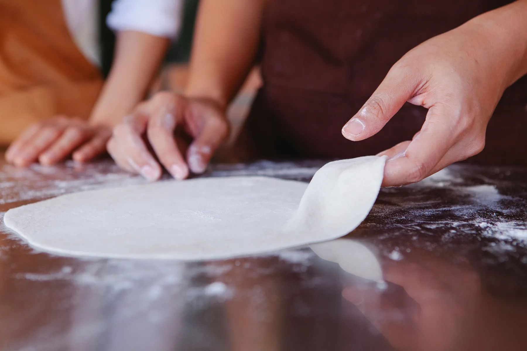 Hands shaping pizza dough on a floured work surface