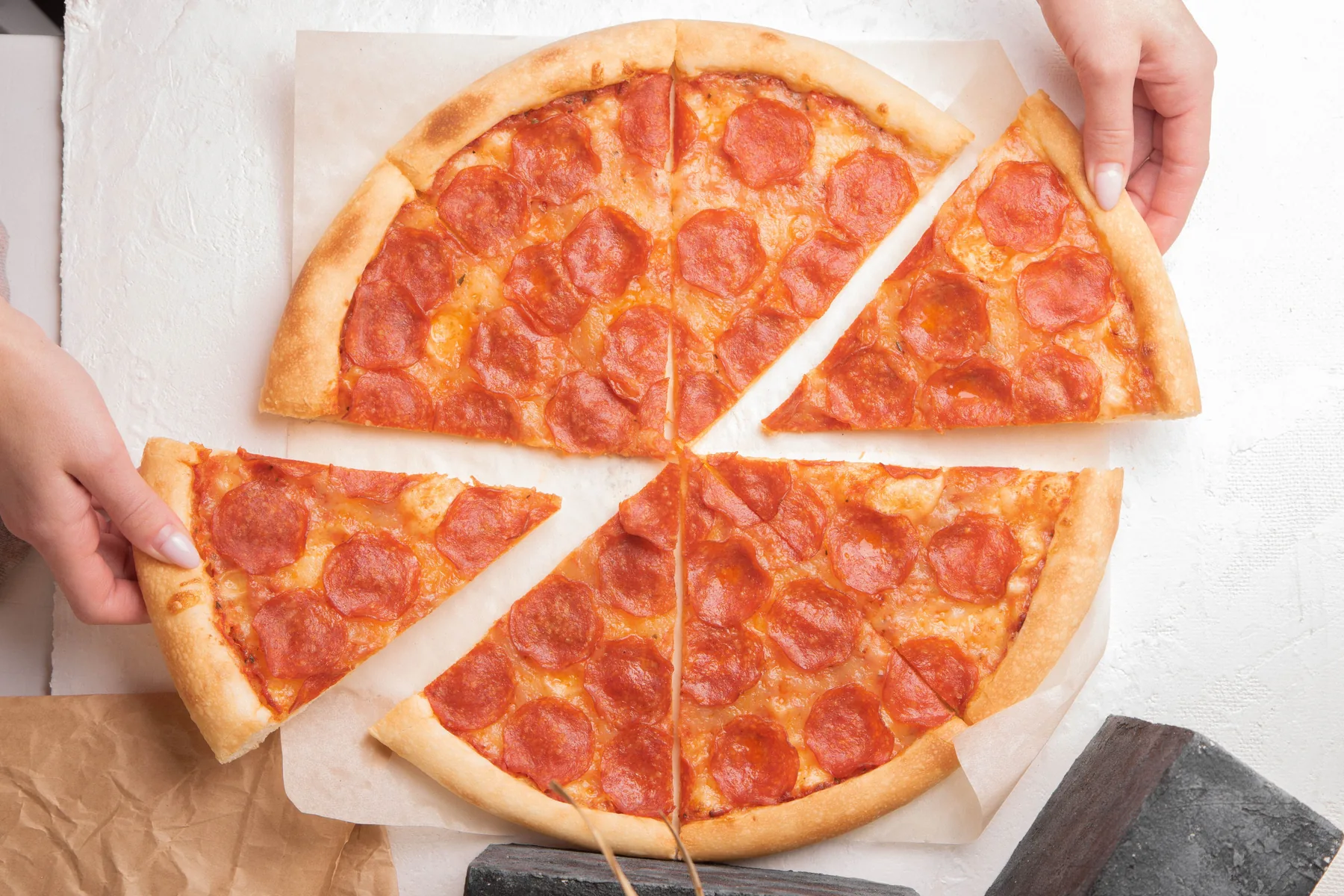 Several hands reaching for slices of pepperoni pizza